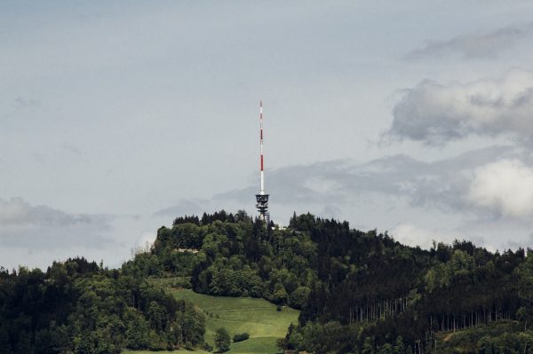 photo of a cell tower erected on a hillside with clouds on the background